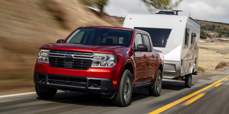 A 2025 a red Ford Maverick truck hauling a rv down a road near Princeton Ford.